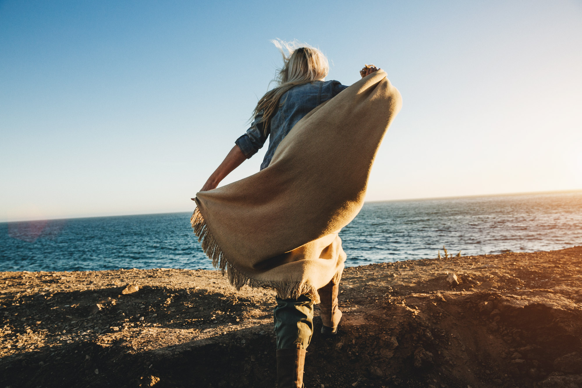 Young woman walking towards the ocean with a blanket